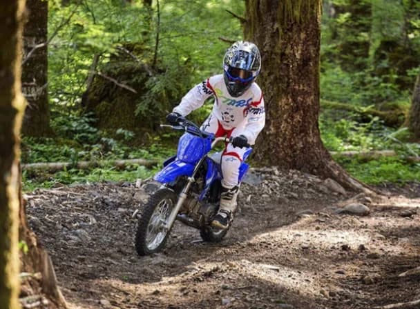 Young rider on a Yamaha TT-R110E cornering on a forest trail